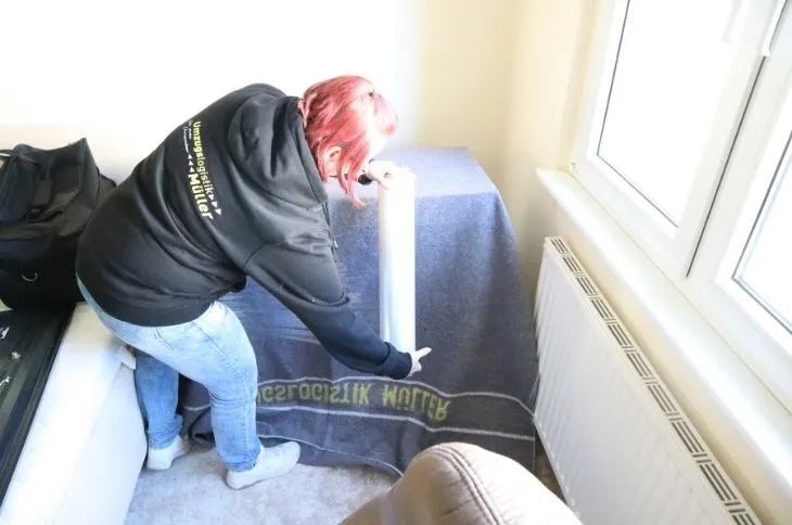 umzugshelferin verpackt moebel mit schutzdecke am fenster